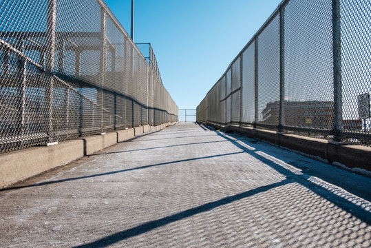 Outdoor overpass ramp walkway with chain link fence. Industrial design and detail.