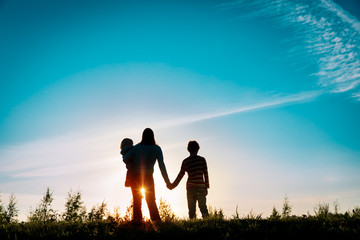 happy mother with son and daughter holding hands in sunset nature