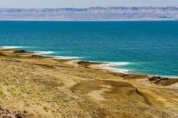 Fototapeta na wymiar Jordan. Dead Sea. Dead Sea coastline in Jordan. Cliffs descend into emerald water of Dead Sea. Closeup of salt crystals along coast. Waves splash to rocks covered with crystals of salt.
