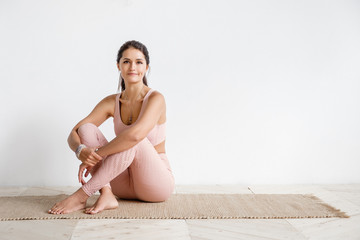 Attractive happy young asian yogi woman working out indoors in white cozy sport class. Side view portrait of beautiful model doing yoga exercise on mat on wooden floor in bright yoga room