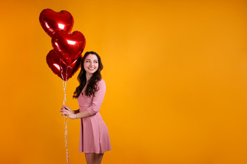 Portrait of young brunette woman posing with helium inflated air balloon. Happy valentine's day concept. Joyful female with wavy hair over colorful background. Close up, copy space for text.