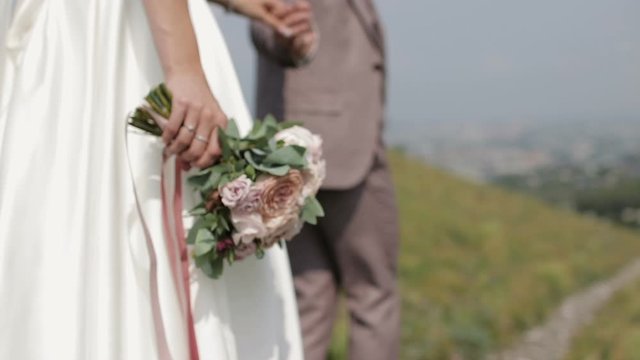 The bride and groom walking, holding hands. Bride carries a bouquet of pink roses