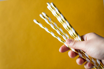 young woman holding gold and white eco paper drinking straws on yellow background