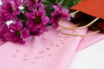  pink chrysanthemum flower on a white background next to a red paper bag, pink cotton napkin on the table, pink sugar hearts scattered