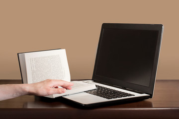 white and black laptop and an open book with young woman's hand on it on a dark wooden table with beige background