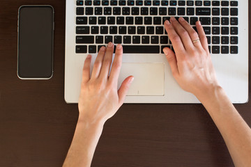 young woman typing on black and white laptop on dark wooden table