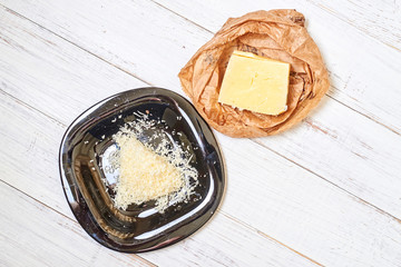 Grated hard cheese on a black plate on a wooden background.