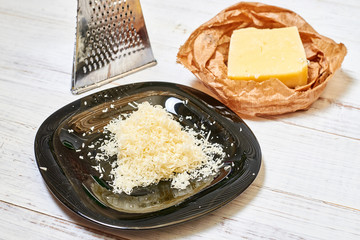 Grated hard cheese on a black plate on a wooden background.