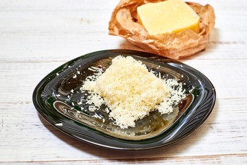Grated hard cheese on a black plate on a wooden background.
