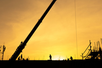 Silhouette sunset construction working and machinery crane hoisting cement mortar mixer bucket container in construction site