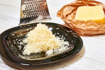 Grated hard cheese on a black plate on a wooden background.