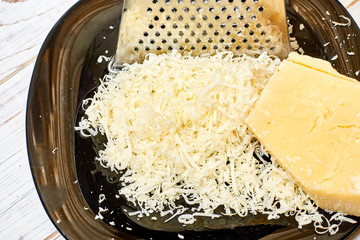 Grated hard cheese on a black plate on a wooden background.