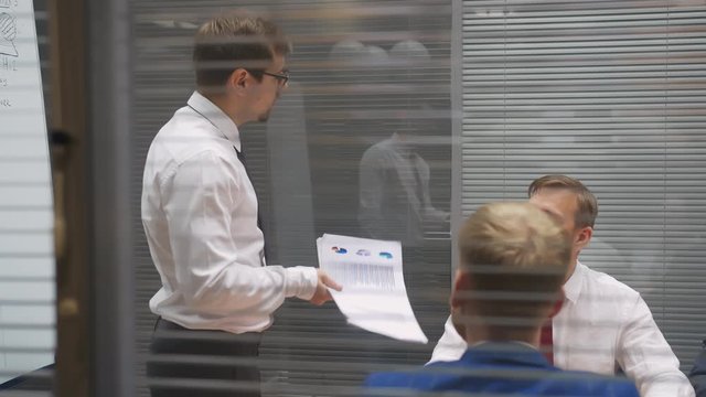Young handsome caucasian businessman makes report presenting documents in front of conference table at meeting room, persuading investors influencing on clients decision with negotiation selling skill