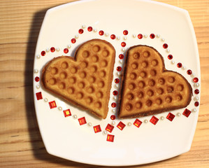 On the plate are two cakes of homemade baking in the form of hearts, decorated with stickers-rhinestones.