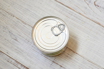 Canned food with a key for opening on a light wooden background.