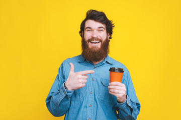 Cheerful bearded hipster man pointing at cup of coffee to go