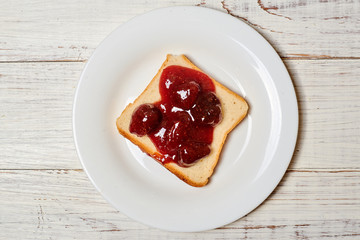 Toast with strawberry jam on a white plate on a light wooden background.