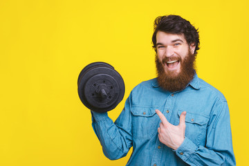 Smiling young bearded man pointing at dumbbell