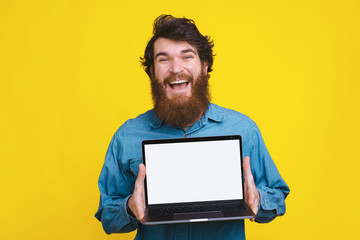 Photo of amazed bearded man showing white screen on laptop