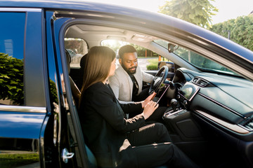 Young African American man communicating with female Caucasian coworker during car drive to business meeting discussing startup ideas and presentation from digital tablet