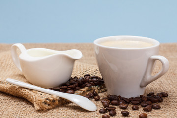 Obraz na płótnie Canvas Cup of coffee, cream and coffee beans on sackcloth