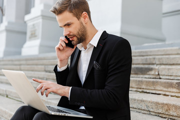 Attractive young businessman wearing suit using mobile phone