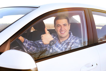 Portrait of young man showing thumbs up sign while driving the car