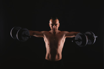 Fototapeta na wymiar Photo of young man doing exercise with dumbbells over dark background