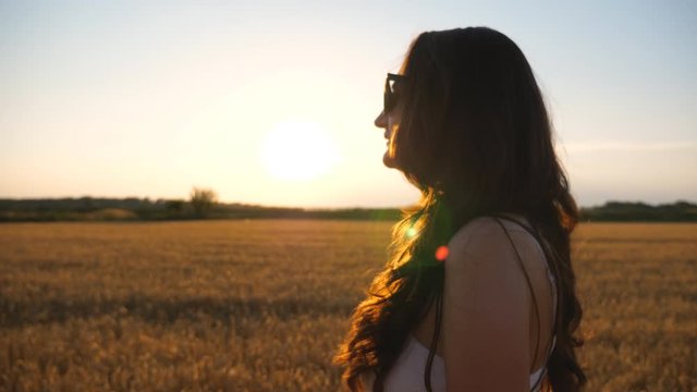 Beautiful woman walking through field of wheat at sunset. Profile of carefree girl enjoying summer evening and freedom in scenic nature environment. Lady strolling at meadow. Side view Close up