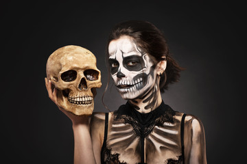 Halloween girl with skull makeup for Halloween on a black background holds a human skull in her...