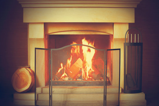 Warm fire in the stone fireplace on a cold night. Warm cozy fireplace with real wood burning in it. Cozy winter concept. Christmas and travel. Christmas backgrounds. Magic burning fireplace. Toning.