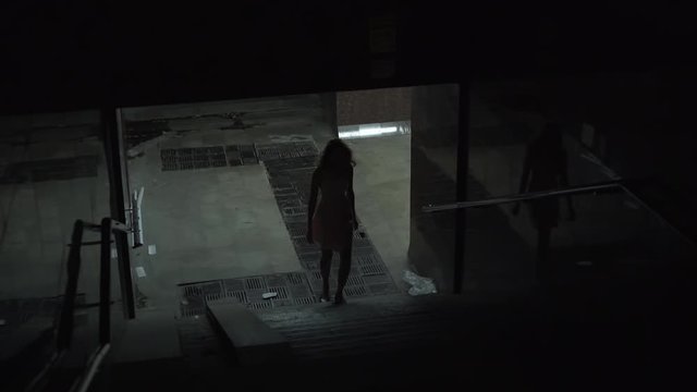 A lonely girl leaves the underpass at night. Dangerous and dirty night quarter, night city. Girls looks around. Feeling of fear and anxiety.