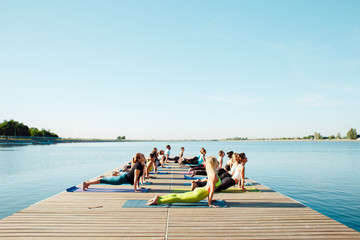 in the morning a group of people do yoga on the pier by the lake