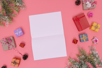 various gift boxes and artificial green plants put around the picture and white paper place in the center. those are placed on a pink background