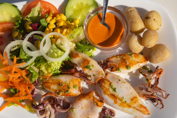 Fototapeta na wymiar Traditional barbecue spanish calamari with salad and potatoes as top view seafood spanish food potato spicy sauce onion rings tomato fish on a table