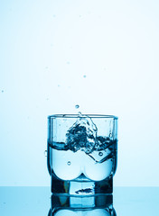 Ice cubes fall into a transparent glass of water and create splashes