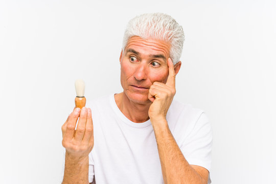 Senior caucasian man recently shaved pointing his temple with finger, thinking, focused on a task.