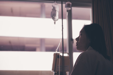 Fototapeta premium young woman sitting on the bed and looking outside window in hospital worry about her illness.