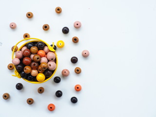 Wooden beads and yellow bucket on white wooden background, Top view with copy space.
