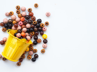 Wooden beads and yellow bucket on white wooden background, Top view with copy space.