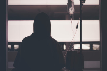 young woman sitting on the bed and looking outside window in hospital worry about her illness.