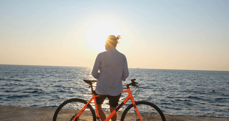 Young handsome male in casual wear ride on the colorful bicycle on the morning beach against beautiful sunset and the sea	