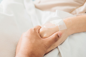 Hand of man hold hands with woman to encourage the patient saline solution lying on the hospital bed. Provide vascular nutrients.