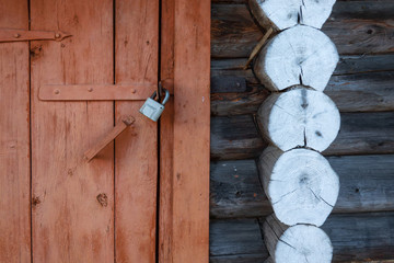 Wall fragment of an old wooden bathhouse building in the countryside. There is a brown door closed to the lock, a gray wall made of logs and white round construction elements. Background. Texture