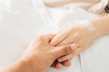 Hand of man hold hands with woman to encourage the patient saline solution lying on the hospital bed. Provide vascular nutrients.