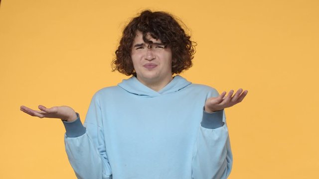 What the hell is that. Slow-motion unimpressed, disappointed young curly guy squinting, looking with dismay and disappointment, shrugging raise hands up frustrated, dont like received order