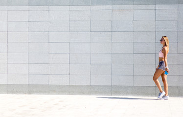 Side view shot of fit young woman walking against grey background. Fit female exercising outdoors in morning.