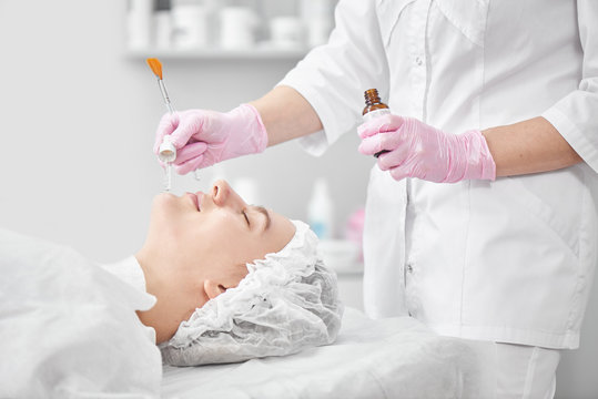 Professional Beautician In Salon Provides Comprehensive Facial Skin Care For Young Woman. Pore Cleansing Procedures, All-season Peeling, Firming Anti-aging Mask