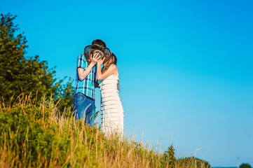 Happy married couple kiss each other behind hat on hill in summer. Blue sky and copy space for...