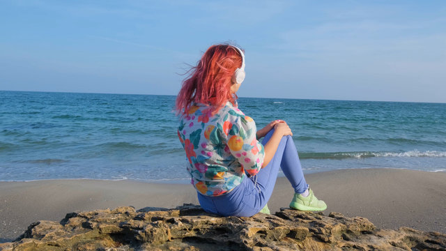 Young woman with colorful hair walk on the summer beach and listen music with headphones	